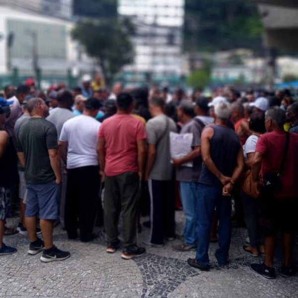 Vista de trás de uma multidão de pessoas reunidas na rua, com foco nas pessoas de camiseta branca e vermelha.