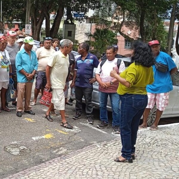 Pessoas reunidas na rua, uma mulher de costas conversa com um homem.